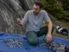 Carabiners, Quickdraws and Belay Devices Explained Climber sorting carabiners, quickdraws and a belay device on a rope tarp before a climb