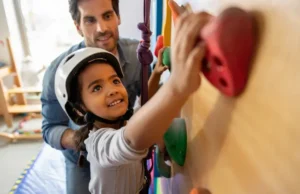 Climber’s Guide: Children’s Climbing Wall Climber parent guiding a young child on a colorful home children's climbing wall, illustrating a climber's guide to fostering this activity.