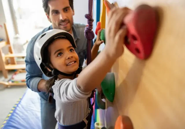 Climber parent guiding a young child on a colorful home children's climbing wall, illustrating a climber's guide to fostering this activity.