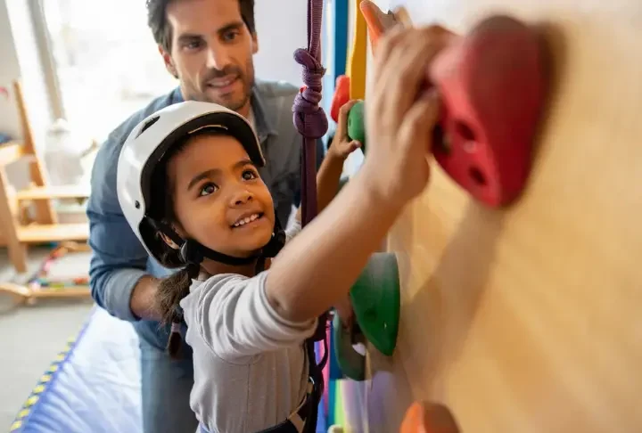 Climber parent guiding a young child on a colorful home children's climbing wall, illustrating a climber's guide to fostering this activity.