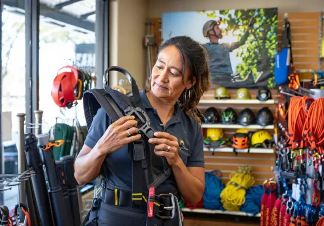 Experienced arborist carefully examining a tree climbing saddle in a specialist store, representing navigating tree climbing stores with arborist secrets.