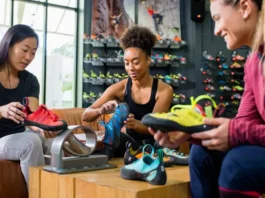 Three diverse women carefully selecting and trying on different models of women's climbing shoes in a well-stocked gear shop, illustrating the ultimate guide to fit and performance.