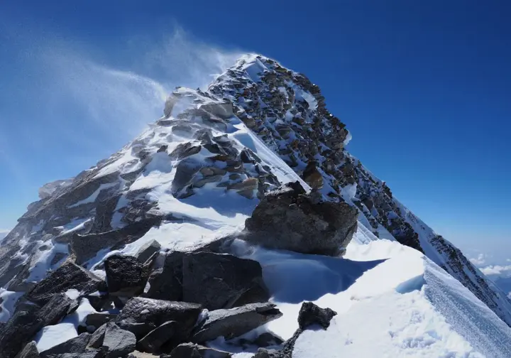 The extreme summit environment on Mount Everest: Windswept snow blowing across the desolate, icy ridge near the peak.