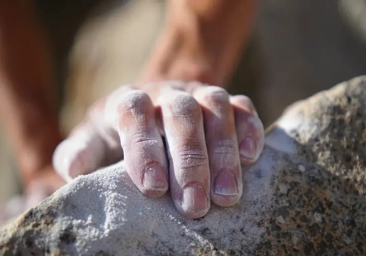 Macro close-up of a climber's chalked fingertips on a granite hold, illustrating the science of climbing chalk and its fundamental role in achieving good grip.