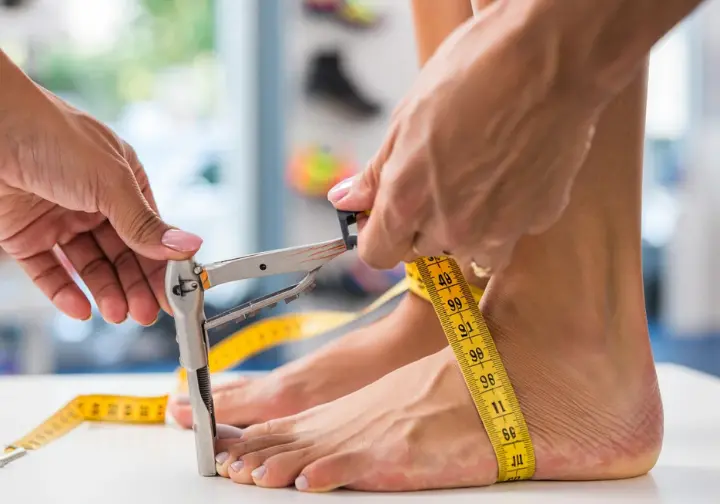 Close-up of a woman's feet being meticulously measured with a Brannock device and tape measure, symbolizing the blueprint for finding the perfect climbing shoe match by understanding unique foot anatomy.