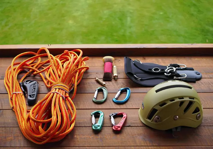 Flat lay of essential tree climbing gear including static rope, arborist saddle, locking carabiners, and helmet, detailing what to look for in stores.