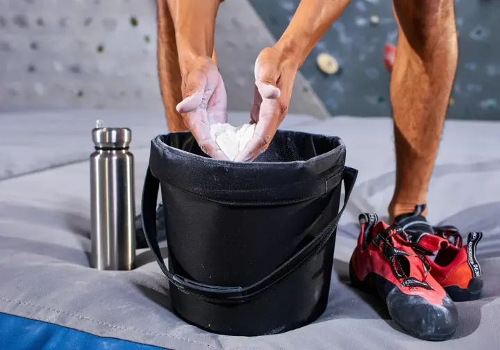 Exploring chalk buckets: A chalk bucket serving as a boulderer's base camp on crash pads in a gym.