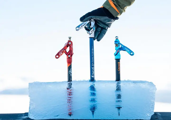 Three top-choice lightest ice screws for 2025 reviewed, placed in a clear block of ice, with a gloved hand evaluating one.