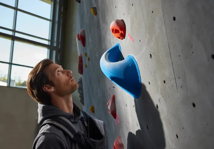 Angler considering key selection factors by comparing different climbing holds next to a home wall.