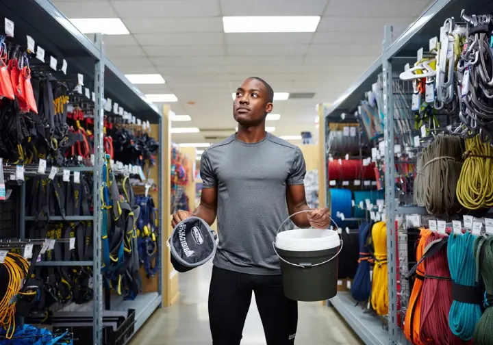 Making your choice: Climber deciding between a chalk bag and a chalk bucket in a gear shop.