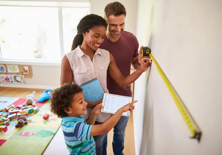 Parents and child planning and designing a children's climbing wall in their home, looking at sketches and a tablet, moving from concept to reality.