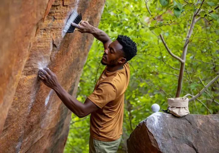 A conscious climber carefully brushing chalk off a rock hold, with eco-friendly chalk accessories nearby, promoting sustainable chalk practices.