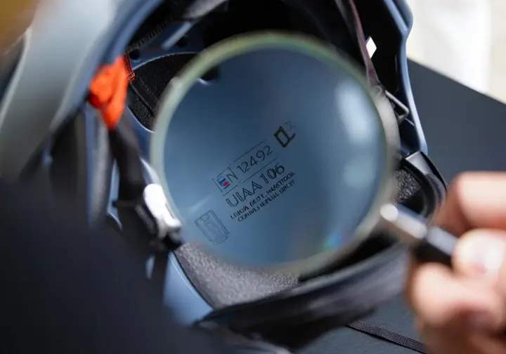 Macro close-up of EN 12492 and UIAA 106 safety standard labels on a climbing helmet, with a magnifying glass nearby, demystifying helmet certifications and prioritizing safety.