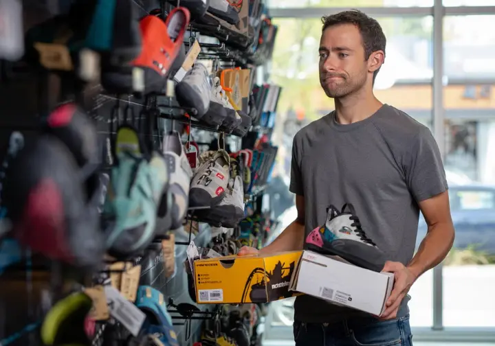 Climber navigating the confusing maze of climbing shoe sizes and brands in a gear shop display.