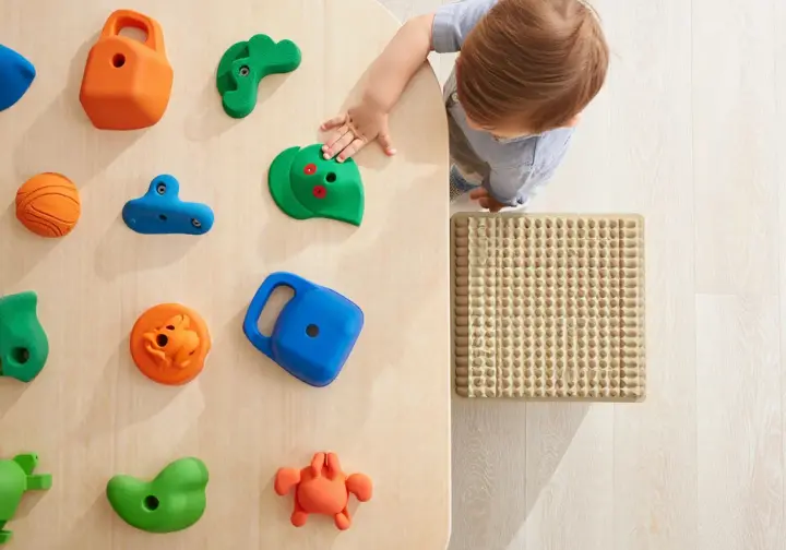 Assortment of colorful, age-appropriate children's climbing holds alongside a section of thick safety surfacing (matting), highlighting essential gear for a children's climbing wall.