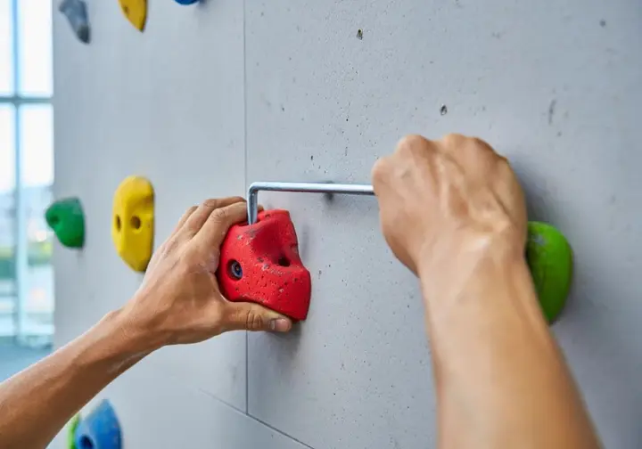 Hands setting a climbing hold onto a home wall panel using a hex wrench and bolt.
