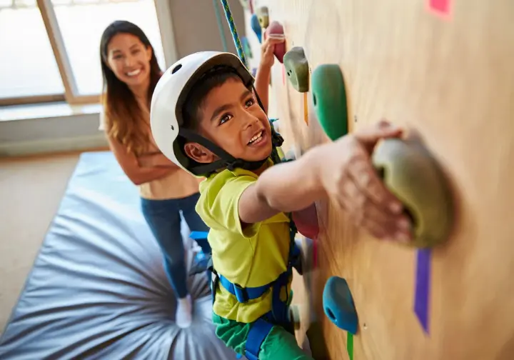 Young child joyfully playing a climbing game on a home children's climbing wall, with a parent guiding and introducing skills, bringing the wall to life.