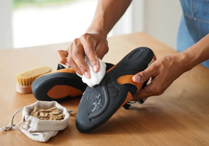 Hands carefully cleaning a pair of women's climbing shoes with a cloth and brush, illustrating tips for caring for and extending the life of climbing footwear.