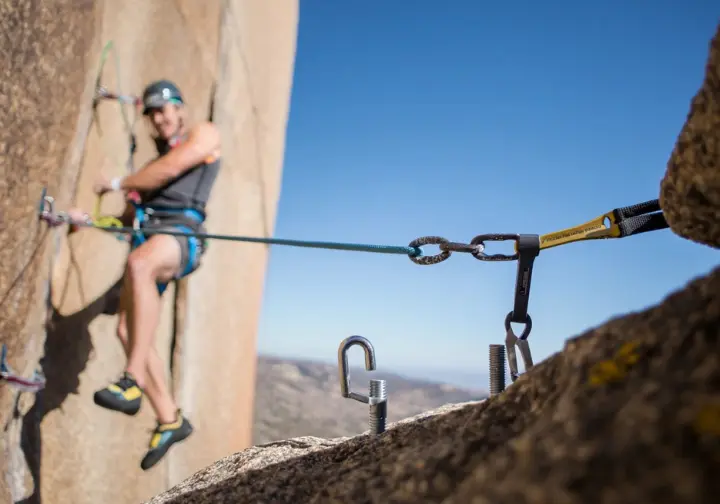 Climber at a belay station demonstrating critical safety for an anchor chain, with their PAS correctly connected to two redundant anchor points with no slack.