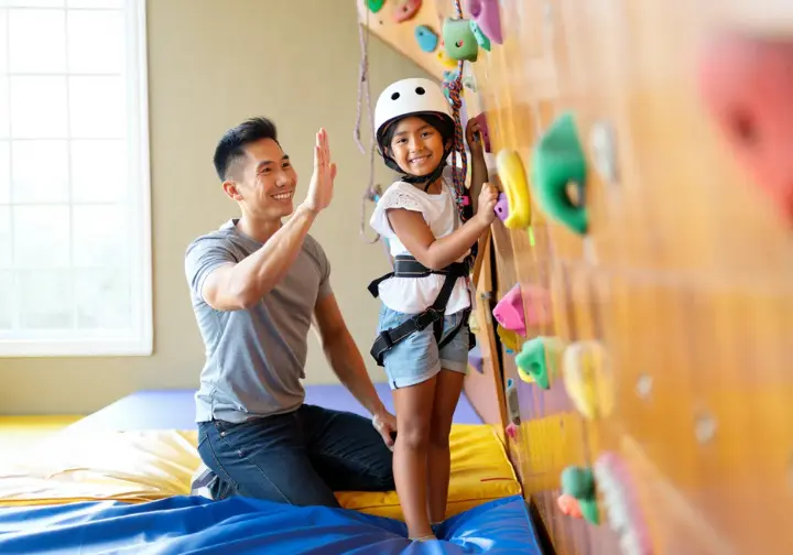 Climber parent giving a high-five and encouragement to their young child on a home children's climbing wall, embodying the parent's role in guiding safely and nurturing passion.