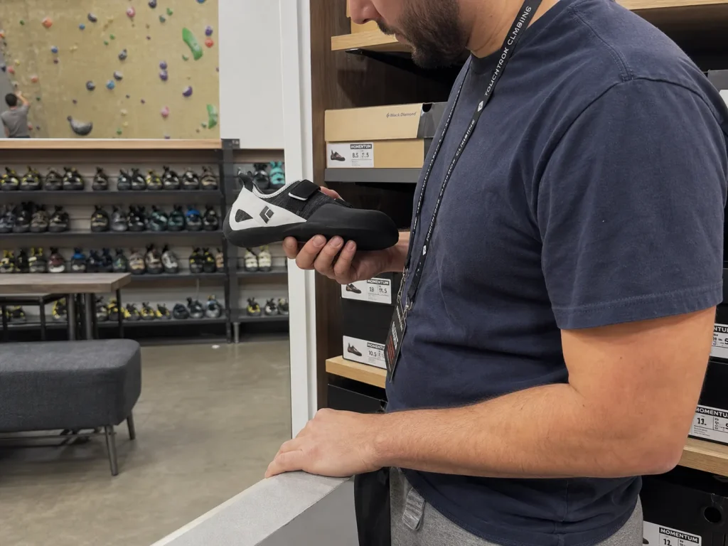 New climber comparing a Black Diamond Momentum shoe against gym rental shoes on a shelf