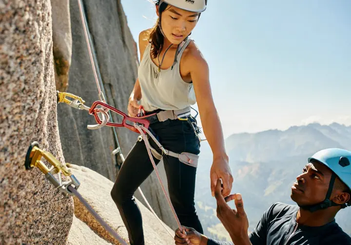 Experienced climber demonstrating best practices for using a PAS (Personal Anchor System) at a multi-pitch belay station to another climber, illustrating expert recommendations for anchor chains.