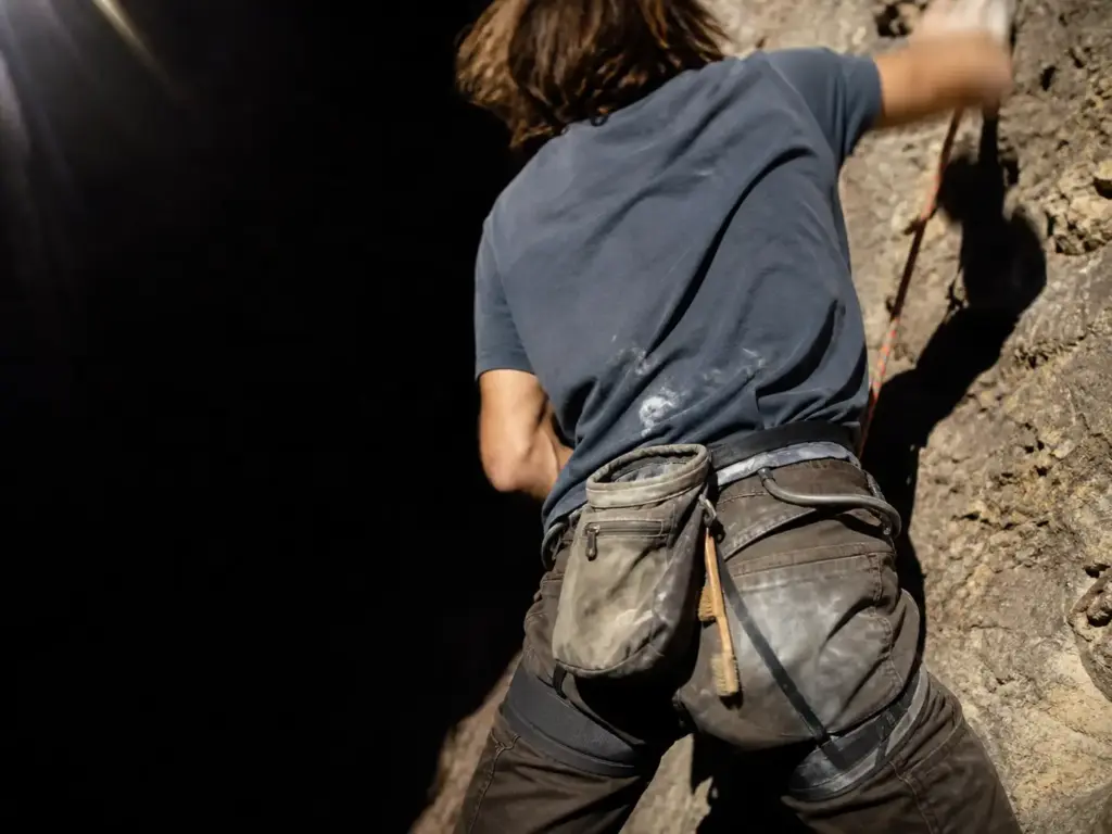 Chalk bag clipped at the back of a climber's harness with the webbing belt and zip pocket visible mid-route