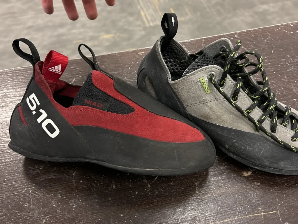 Close-up of a leather slip-on Five Ten Niad Moccasym beside a laced climbing shoe on a bench