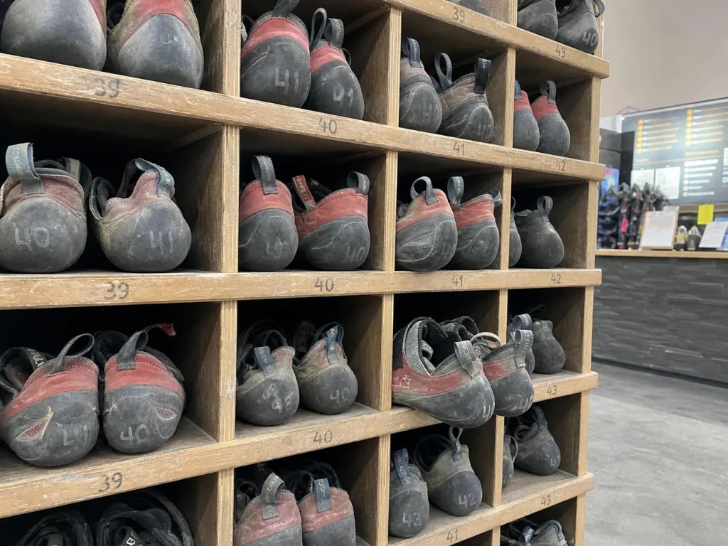 Rows of worn communal rental climbing shoes in gym cubbies with numbers on the heels