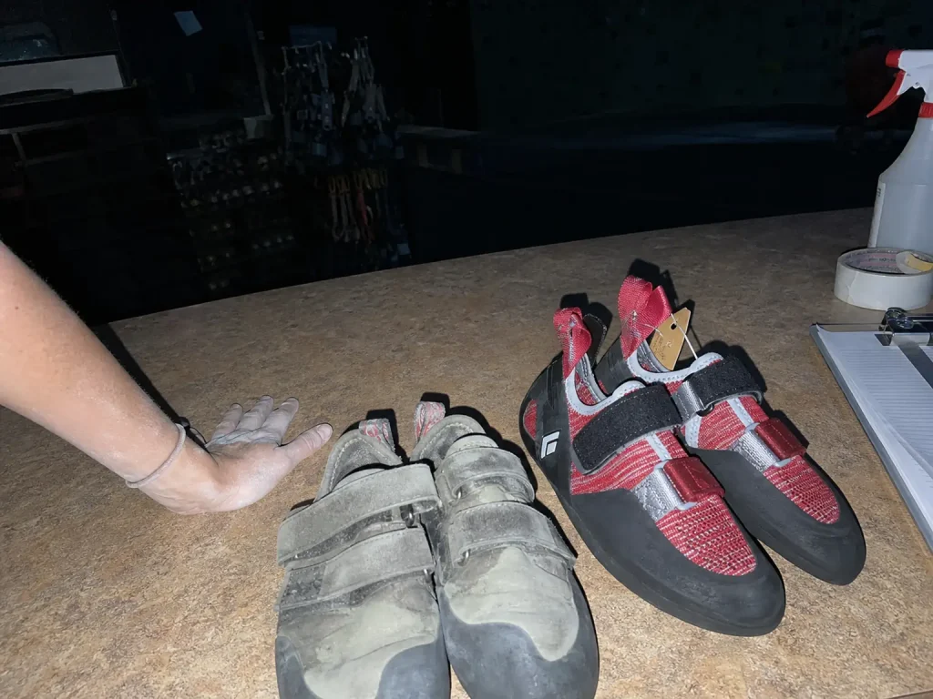 Rental climbing shoes on a gym counter beside a new pair of Black Diamond Momentum women's shoes
