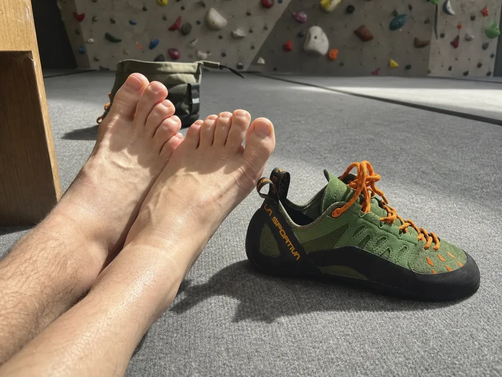Bare feet resting beside a La Sportiva Tarantulace climbing shoe taken off between climbs
