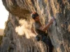 Best Climbing Chalk: Field-Tested for Grip & Skin Climber on a steep limestone route reaching into chalk bag, creating a cloud of chalk dust in the sunlight.