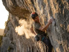 Best Climbing Chalk: Field-Tested for Grip & Skin Climber on a steep limestone route reaching into chalk bag, creating a cloud of chalk dust in the sunlight.