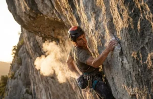 Best Climbing Chalk: Field-Tested for Grip & Skin Climber on a steep limestone route reaching into chalk bag, creating a cloud of chalk dust in the sunlight.