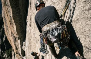Best Climbing Harnesses: Field-Tested & Racked (2026) A climber suspended in a harness at a high-altitude hanging belay, gear loops fully racked with traditional climbing equipment.