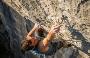 Carabiner Selection: Physics, Safety & Rack Strategy Climber reaching to clip a quickdraw into a bolt on a steep rock wall during a lead climb.