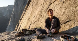 Climbing Gear Checklist: The Gym to Crag Roadmap A climber gearing up at the base of a cliff, surrounded by a rope, quickdraws, and a helmet on a tarp.
