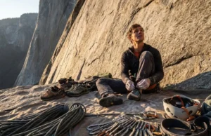 Climbing Gear Checklist: The Gym to Crag Roadmap A climber gearing up at the base of a cliff, surrounded by a rope, quickdraws, and a helmet on a tarp.