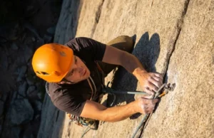 Climbing Helmet Guide: Best Picks by Head Shape & Tech A climber wearing a modern climbing helmet ascending a steep granite rock face during sunset.