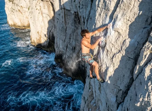 damian-cook-dws-climber-life A climber deep water soloing on a steep limestone cliff above the ocean, representing the sport Damian Cook pioneered.
