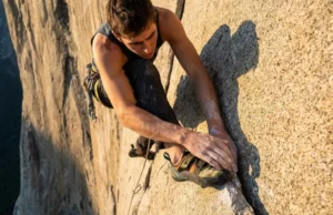 Scarpa Climbing Shoes: Families, Fit & Rubber Guide A climber on a granite wall looking down at their yellow and black Scarpa climbing shoe edging on a small rock crystal