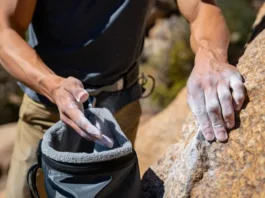 Climber's hands gripping a rock hold and dipping into a chalk bag, illustrating the importance of choosing chalk and chalk bags wisely for better grip.