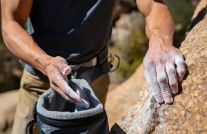 Grip Up: Choosing Your Chalk Bag and Chalk Wisely Climber's hands gripping a rock hold and dipping into a chalk bag, illustrating the importance of choosing chalk and chalk bags wisely for better grip.