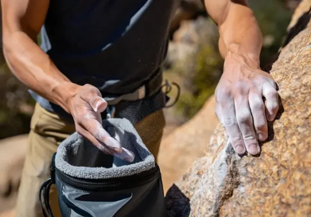 Climber's hands gripping a rock hold and dipping into a chalk bag, illustrating the importance of choosing chalk and chalk bags wisely for better grip.