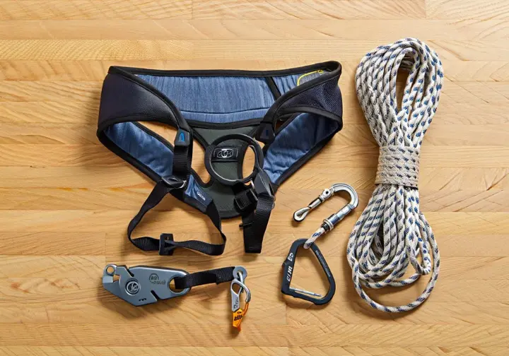 Flat lay of essential belay system components: climbing harness, rope, belay device, and locking carabiner, illustrating the foundations of belaying for a safe belay in climbing.