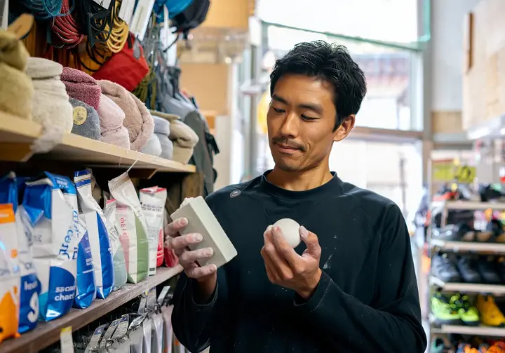Climber in a gear shop thoughtfully comparing different types of climbing chalk and chalk bags, illustrating how to select the right gear.