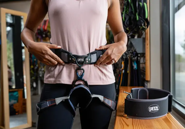 Climber carefully adjusting the waistbelt of a Petzl climbing harness to achieve a correct and secure fit, illustrating proper sizing techniques.