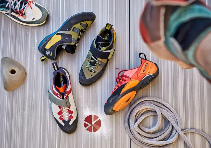 Flat lay of several top-rated beginner rock climbing shoes for 2025, with a subtle crossed-out sneaker in the background, emphasizing forgetting sneakers for climbing