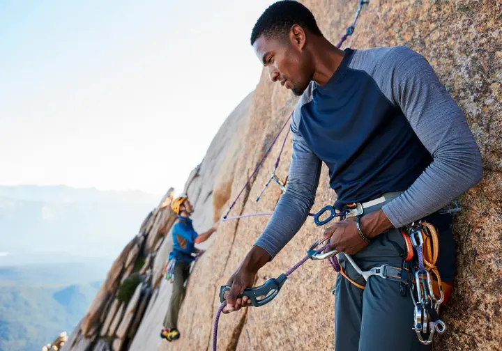 Experienced climber belaying from above in guide mode on a multi-pitch route, with an Edelrid OHM visible, illustrating advanced belaying considerations and specialized skills.