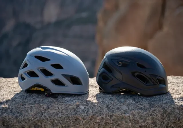 Two rock climbing helmets, one lightweight and one durable, resting on a rock surface, illustrating the choice between lightweight and durable rock climbing helmets.